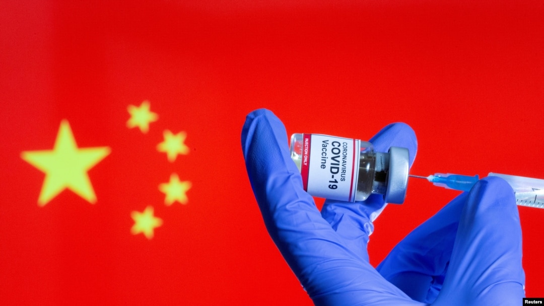 A woman holds a small bottle labeled with a "Coronavirus COVID-19 Vaccine" sticker and a medical syringe in front of displayed China flag, Oct. 30, 2020.