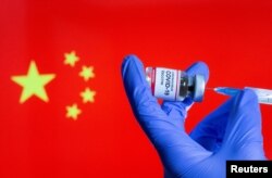 A woman holds a small bottle labeled with a "Coronavirus COVID-19 Vaccine" sticker and a medical syringe in front of displayed China flag, Oct. 30, 2020.
