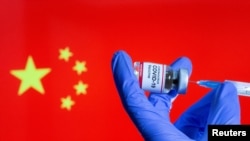 A woman holds a small bottle labeled with a "Coronavirus COVID-19 Vaccine" sticker and a medical syringe in front of displayed China flag, Oct. 30, 2020.