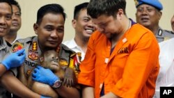 Kapolresta Denpasar, Ruddi Setiawan (Kiri Tengah) menggendong orangutan jantan berusia dua tahun saat Andrei Zhestkov (kanan), tertuduh penyelundup hewan langka berbicara dalam konferensi pers di Bali, Indonesia, 25 Maret 2019 (foto: AP Photo/Firdia Lisnawati)