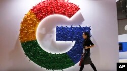 FILE - A woman walks past the logo for Google at the China International Import Expo in Shanghai, Nov. 5, 2018.