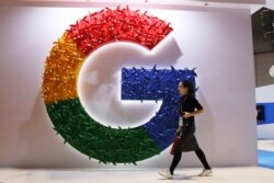 FILE - A woman walks past the logo for Google at the China International Import Expo in Shanghai, Nov. 5, 2018.