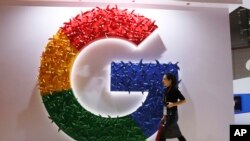FILE - A woman walks past the logo for Google at the China International Import Expo in Shanghai, Nov. 5, 2018.