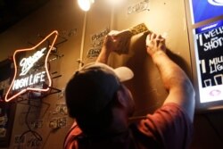 General manager David Hartley removes one dollar bills from the wall at the Boar's Head Lounge in downtown Athens, Ga, April 16, 2020.