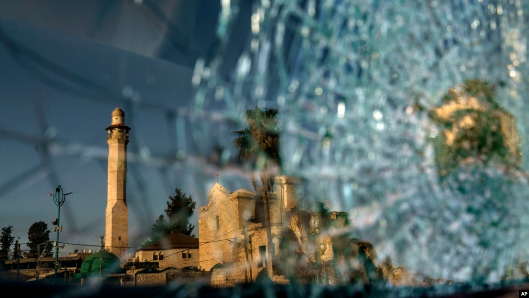 The minaret of the Al-Omari mosque and St. George Greek Orthodox church are reflected in the broken windshield of a vehicle sitting outside a synagogue in the mixed Arab-Jewish town of Lod, central Israel, Wednesday, May 26, 2021.(AP Photo/David Goldman)