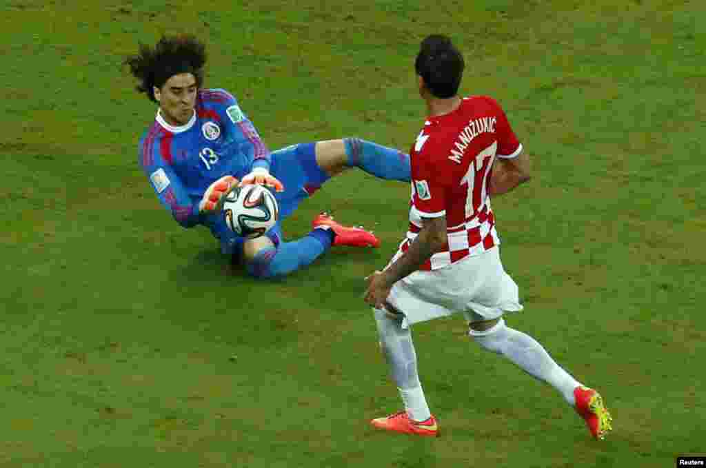 Penjaga gawang Meksiko Guillermo Ochoa berhasil menangkap bolah di depan pemain Kroasia Mario Mandzukic dalam pertandingan di Pernambuco Arena di Recife, 23 Juni 2014.