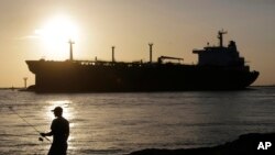 FILE - An oil tanker passes a fisherman as it enters a channel near Port Aransas, Texas, July 21, 2015, heading for the Port of Corpus Christi. 