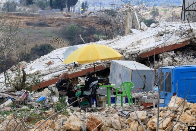 Orang-orang duduk mengelilingi meja yang didirikan di atas reruntuhan rumah mereka yang hancur selama perang baru-baru ini antara Israel dan Hizbullah, di desa al Jibbain di Lebanon selatan, pada 31 Januari 2025. (Foto: AFP)