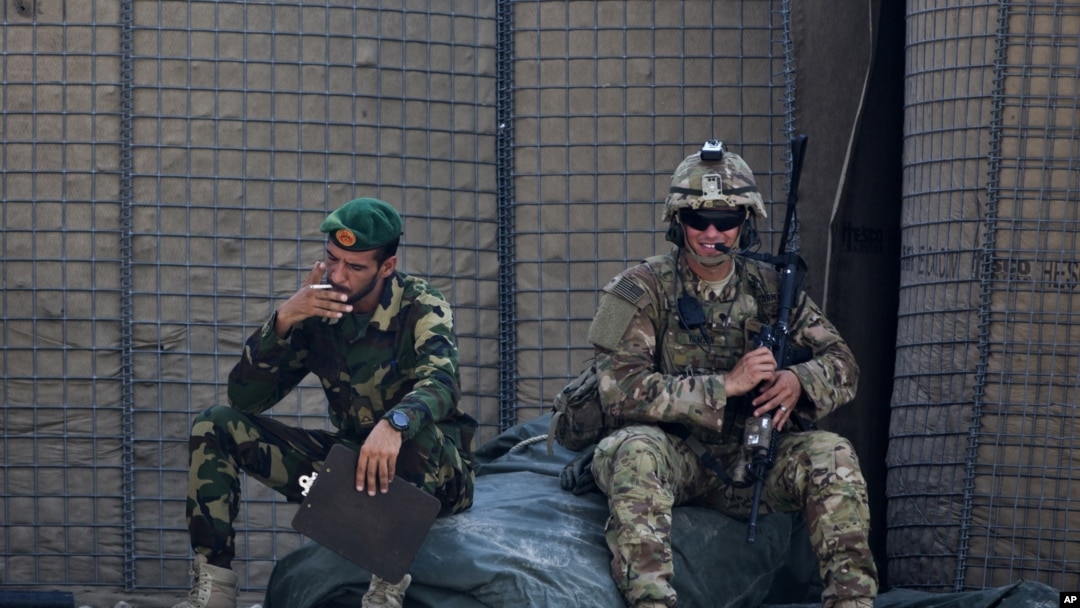 FILE - In this Aug. 5, 2015 photo, an Afghan National Army soldier, left, smokes as a U.S. Army soldier from Charlie Company, 2-14 Infantry Regiment, 2nd Brigade, 10th Mountain Division sits next to him in Camp Khogyani in Nangarhar province, east of Kabul, Afghanistan. 