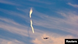 Sebuah jejak pesawat tampak di antara awan dan di atas sebuah pesawat yang baru lepas landas dari Bandara Sydney, Sydney, Australia, 5 Juni 2017 (foto: REUTERS/David Gray)