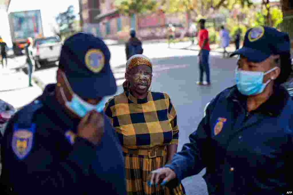A woman reacts in pain after being pepper sprayed by a member of the South African Police Service, not visible, for not wearing a face mask, as members of the Johannesburg Metro Police Department walk away, in Hillbrow, Johannesburg.