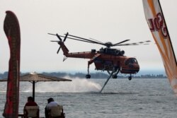 An helicopter fills with water as people watch from the beach during a wildfire at Pefki village on Evia island.
