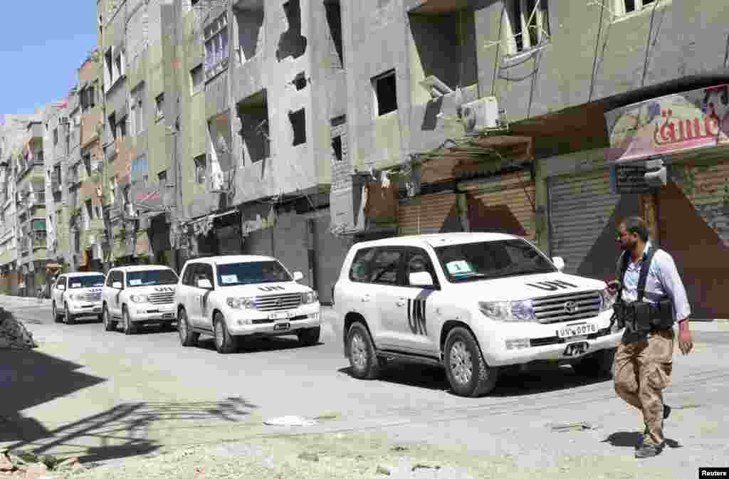 A Free Syrian Army fighter passes by the convoy of U.N. vehicles carrying chemical weapons experts at the site of an alleged chemical weapons attack in a Damascus suburb, August 28, 2013. 