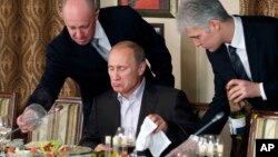 FILE - In this Nov. 11, 2011, photo, businessman Yevgeny Prigozhin, left, serves food to Russian Prime Minister Vladimir Putin, center, during dinner at Prigozhin's restaurant outside Moscow. 