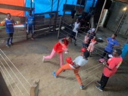 Two women in a boxing training session in Katanga Slum as Hellen Baleke outside the ring looks on.