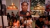 FILE - Book lovers read beneath poster promoting "Stange Leung Chun-ying," which depicts the new Hong Kong Chief Executive as the late Chinese leader Mao Zedong, Hong Kong Book Fair, July 18, 2012.