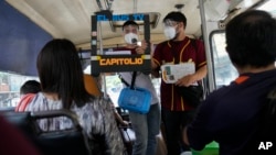 Juan Pablo Lares, right, holds a cardboard frame in front of his associate Maximiliano Bruzual who reads their newscast "El Bus TV Capitolio" to commuters on a bus in Caracas, Venezuela. (AP Photo/Ariana Cubillos)