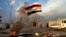 Un manifestante ondea una bandera iraquí mientras otros bloquean las calles con fuego cerca de la plaza Tahrir en Bagdad, Irak, el miércoles, 8 de enero de 2020.