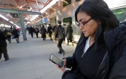 FILE - Marilu Rodriguez checks a news website on her smartphone before boarding a train home at the end of her workweek in Chicago, March 13, 2015.