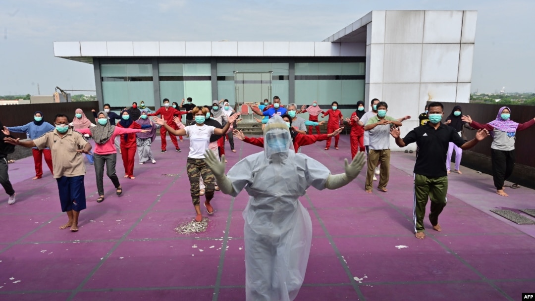 A gymnastics instructor wearing personal protective equipment (PPE) leads a morning exercise for patients of the COVID-19 coronavirus at a hotel designated to treat asymptomatic patients in Karawaci, Indonesia's Banten province, on October 5, 2020. 