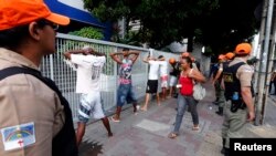 Seorang perempuan berjalan melewati para pengunjuk rasa yang ditahan karena vandalisme, sementara para petugas kepolisian berjaga, Recife City, Brazil, 20 Juni 2013.