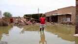 FILE - A man gestures as he wades through a flooded road in the town of Salmaniya, about 35 km southwest of the capital, Khartoum, Sudan, Sept. 17, 2020.