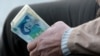 FILE- In this Thursday, Jan. 26, 2012 file photo, an Iranian street money changer holds Iranian banknotes with a portrait of late revolutionary founder Ayatollah Khomeini, in the main old Bazaar of Tehran, Iran. President Mahmoud Ahmadinejad blamed…