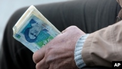 FILE- In this Thursday, Jan. 26, 2012 file photo, an Iranian street money changer holds Iranian banknotes with a portrait of late revolutionary founder Ayatollah Khomeini, in the main old Bazaar of Tehran, Iran. President Mahmoud Ahmadinejad blamed…