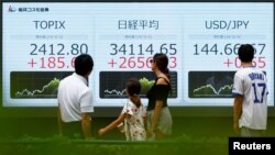 Passersby look at an electronic board displaying Topix, Japan's Nikkei share averages, and Japanese yen exchange rate against the U.S. dollar outside a brokerage in Tokyo, Japan, Aug. 6, 2024.