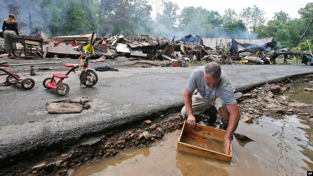 Mark Lester membersihkan kotak dengan air sungai kecil menyusul banjir parah di White Sulphur Springs, West Virginia (24/6). (AP/Steve Helber)