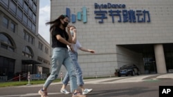 资料照片：在北京，行人戴着口罩走过拥有抖音/TikTok的字节跳动公司的总部。(2020年8月7日)