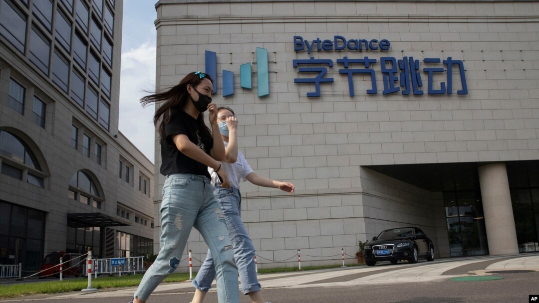 In this Aug. 7, 2020, file photo, women wearing masks to prevent the spread of the coronavirus chat as they pass by the headquarters of ByteDance, owners of TikTok, in Beijing, China. 