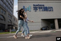 FILE - In this Aug. 7, 2020, photo, women wearing masks to prevent the spread of the coronavirus chat as they pass by the headquarters of ByteDance, owners of TikTok, in Beijing, China.