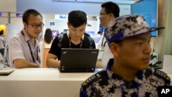 FILE - Visitors use a laptop computer at a display booth as a security guard stands nearby at the Global Mobile Internet Conference in Beijing, April 29, 2015.