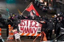 FILE - A protester carries a flag that reads "Antifascist Action" near a banner that reads "Justice for Manny," during a protest against police brutality, in downtown Tacoma, Wash., Jan. 24, 2021.