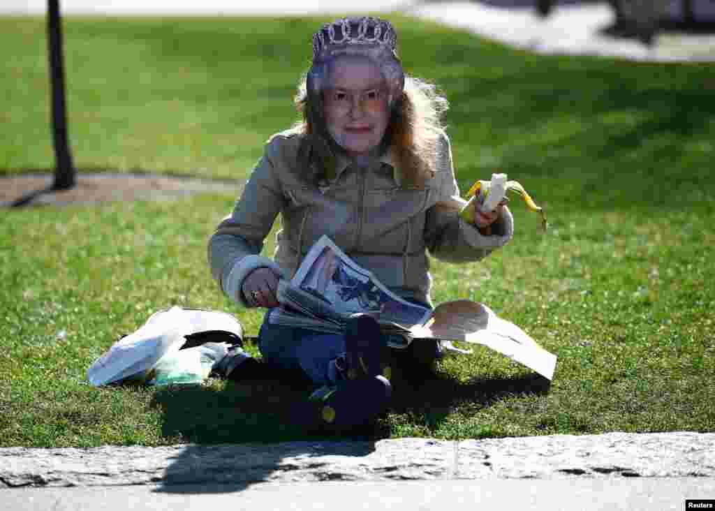 A woman wearing a mask of Britain&#39;s Queen Elizabeth reads a newspaper near Tower Bridge in London.