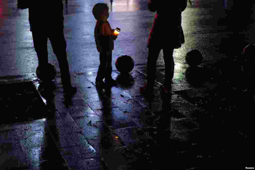 A boy holding a lit candle looks at his mother while they attend an event to commemorate the 65 victims of the Colectiv fire, in Bucharest, Romania, Oct. 30, 2020.
