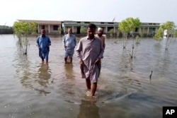 Villagers wade through floodwaters caused by heavy monsoon rains near Sohbat Pur, an area of Pakistan's southwestern Balochistan province, on Aug. 19, 2024.