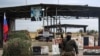 A Syrian rebel fighter stands at a checkpoint next to a Russian flag and a portrait of President Vladimir Putin at the entrance of the Russian-leased Syrian military base of Hmeimim in Latakia province, western Syria, Dec. 29, 2024.