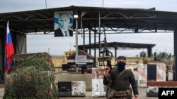 A Syrian rebel fighter stands at a checkpoint next to a Russian flag and a portrait of President Vladimir Putin at the entrance of the Russian-leased Syrian military base of Hmeimim in Latakia province, western Syria, Dec. 29, 2024.