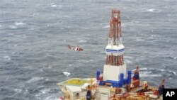 Dari foto yang dirilis oleh Pengawas Pantai Amerika ini, nampak sebuah helikopter dari pangkalan Kodiak tengah memberikan instruksi kepada 18 awak anjungan nomor 13 pengeboran minyak Kulluk (29/12). Anjungan milik perusahaan minyak Shell ini terlepas dari kapal yang menanganinya di laut yang berombak besar Teluk Alaska pada Malam Tahun Baru, dan kandas di pantai berbatu-batu pulau Sitkalidak.