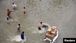 FILE - A volunteer (R) transporting boxes of food supplies on an inflatable raft, falls into the water after being pushed by a man (2nd R) as other people look on, on a flooded street during a supply shortage after Typhoon Fitow hit Yuyao, October 9, 2013. 