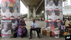 People sits under campaign posters of Lagos State Governorship candidate of the All Progressives Congress party, Akinwunmi Ambode, on the street in Lagos, Nigeria, April 10, 2015.