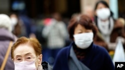 FILE - Pedestrians wear protective masks in Tokyo, Jan. 16, 2020. Japan's government said a man treated for pneumonia after returning from China has tested positive for the new coronavirus identified as a possible cause of an outbreak in Wuhan, China.
