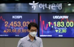 A currency trader walks near screens showing the Korea Composite Stock Price Index (KOSPI), left, and the foreign exchange rate between U.S. dollar and South Korean won at the foreign exchange dealing room in Seoul, Aug. 13, 2020.