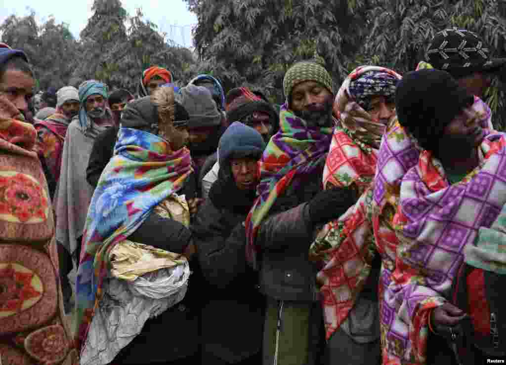 Homeless men stand in a line on the side of a street to collect food on a cold winter morning in the old quarters of Delhi, India.