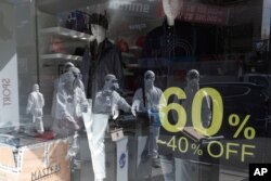 Workers wearing protective gear are reflected in a window of a store as they prepare to spray disinfectant as a precaution against the coronavirus in a shopping district in Seoul, South Korea, Feb. 27, 2020.
