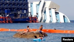 People sunbathe near the capsized cruise liner Costa Concordia lying surrounded by cranes outside Giglio harbor, Italy, July 17, 2013. 