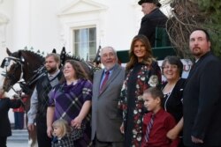 First lady Melania Trump poses with the 2019 White House Christmas tree as it is delivered to the White House in Washington, Nov. 25, 2019. The tree came from the Pennsylavia farm of Larry Snyder, third from left, pictured here with his family.