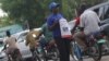 A stream of boda bodas passes a woman holding a poster advertising the launch of a new VOA frequency in Juba in March 2013.